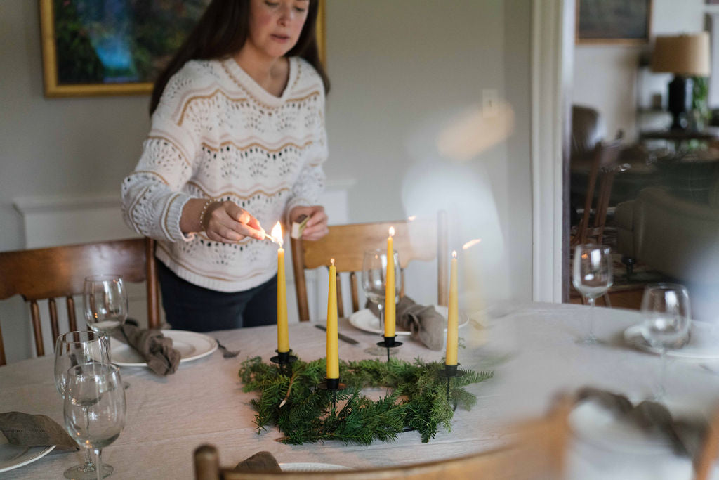 Woman lighting a table wreath of four beeswax candles with a match.