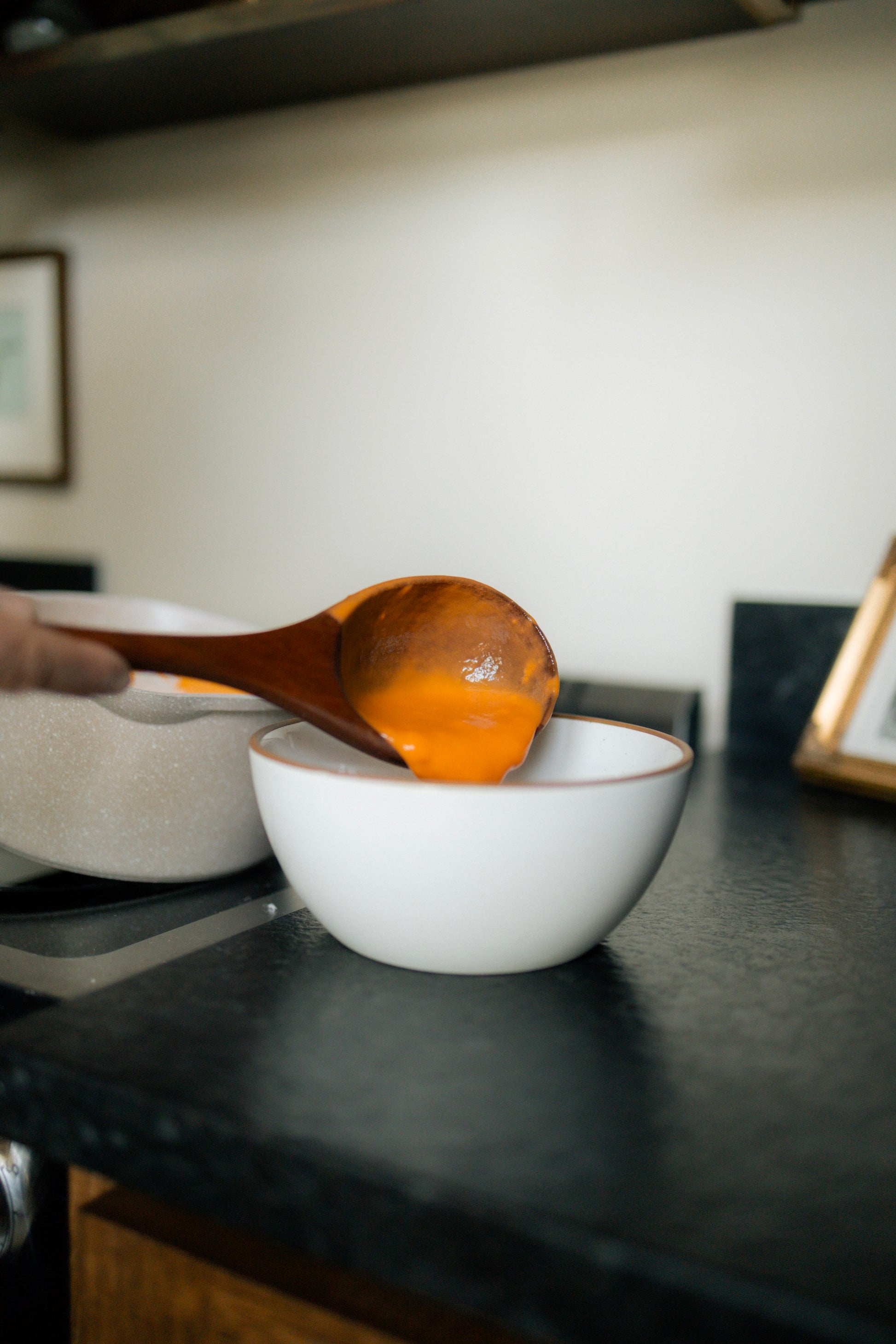 Cherry wooden ladle pouring soup into white bowl.