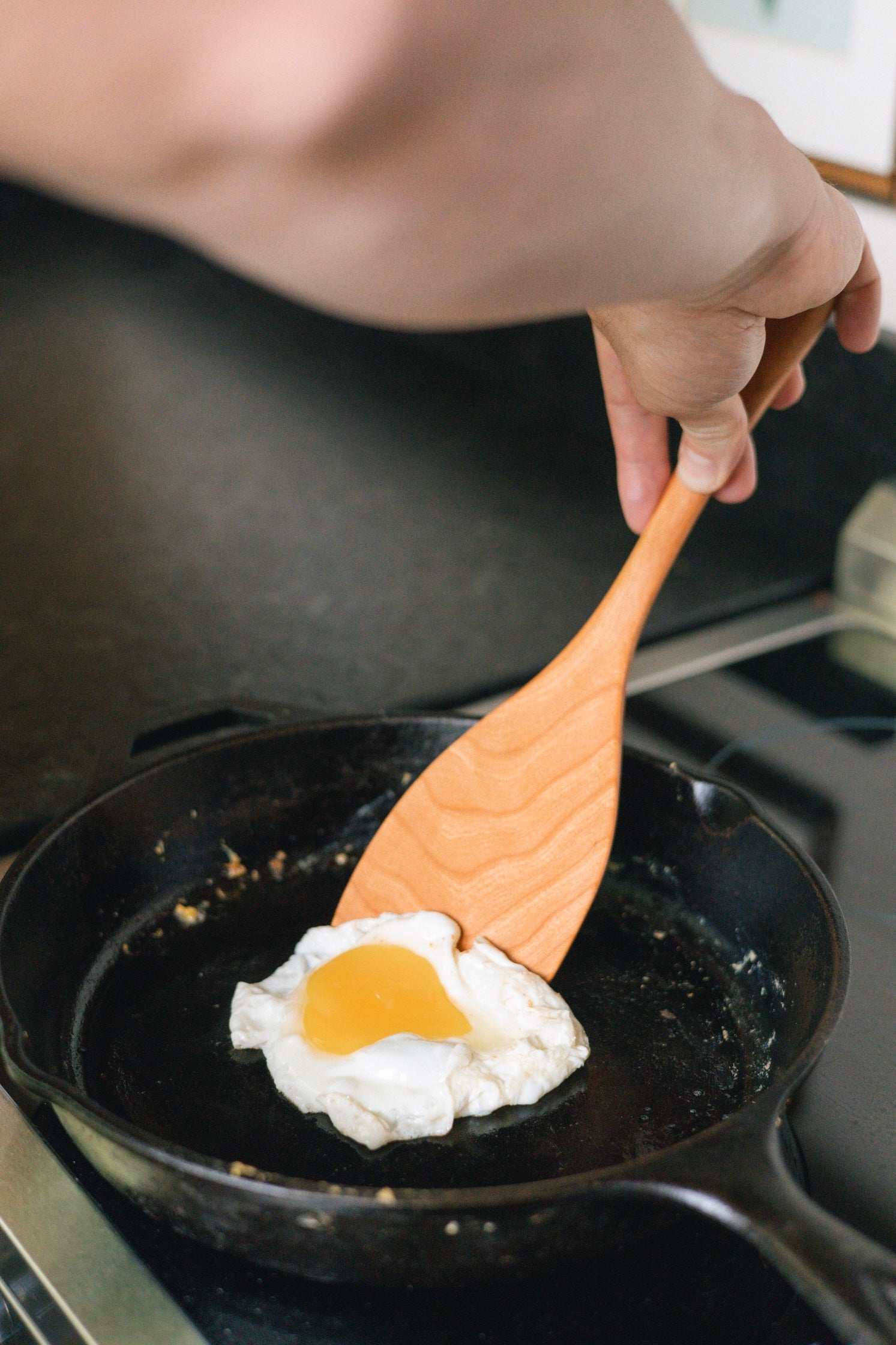 Flipping an egg using large cherry wood spatula in cast iron pan.