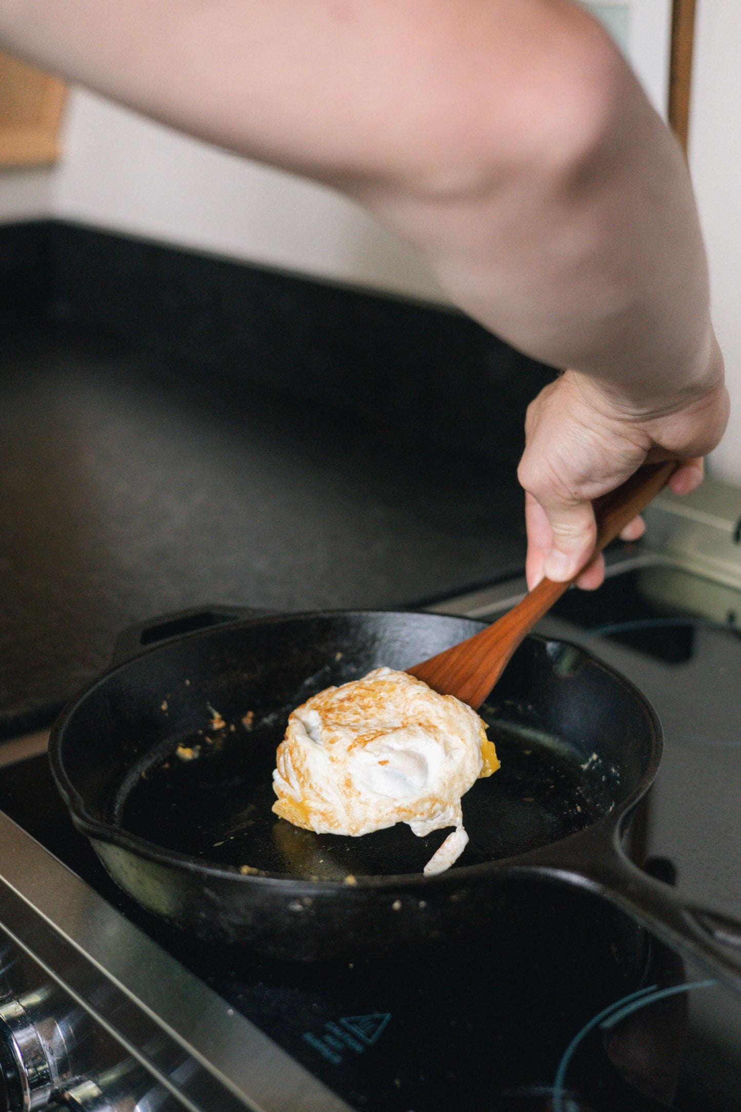 Flipping egg in cast iron pan using large cherry wood spatula.