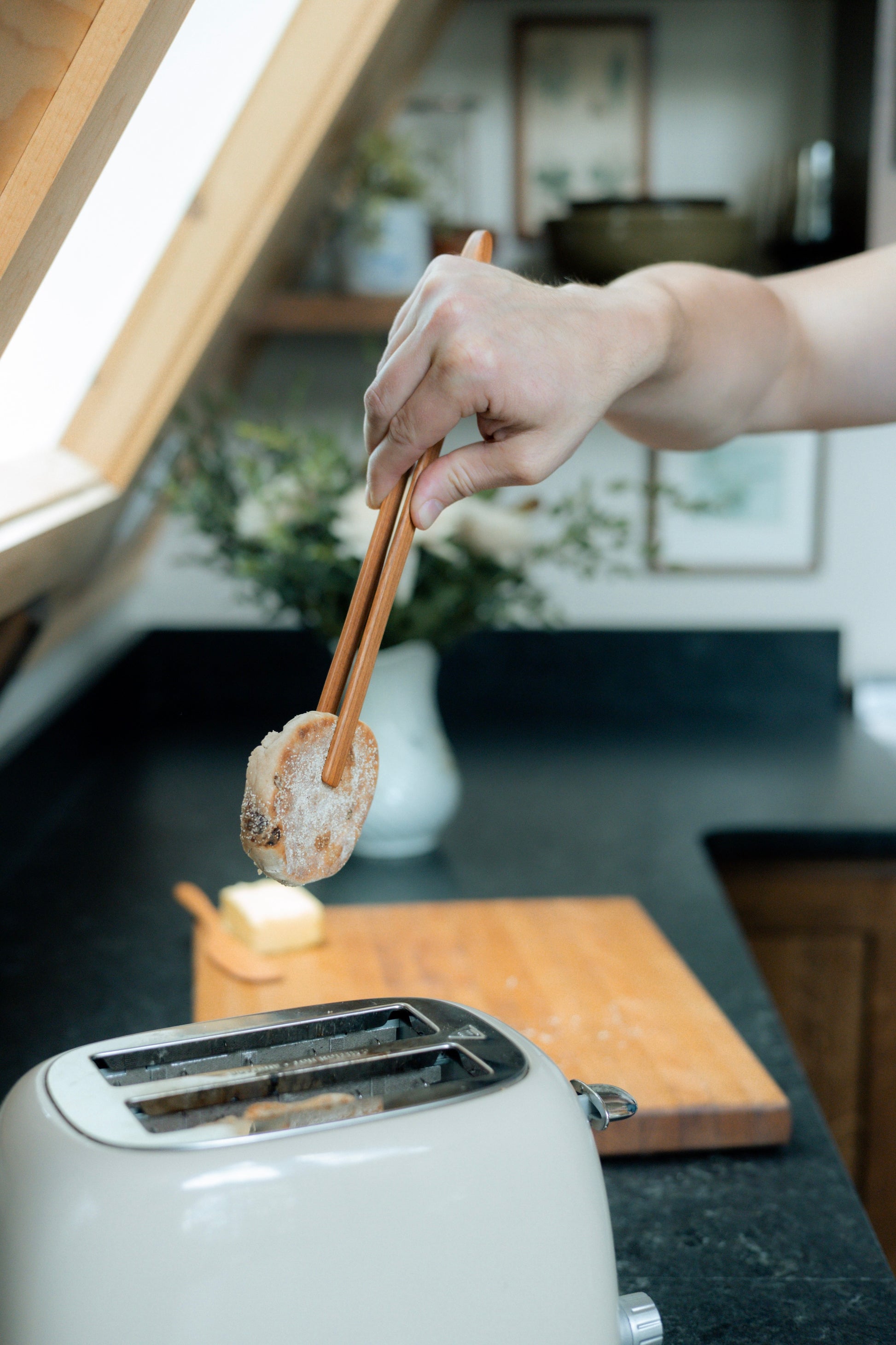 Using cherry wooden tongs to take english muffin out of white toaster.