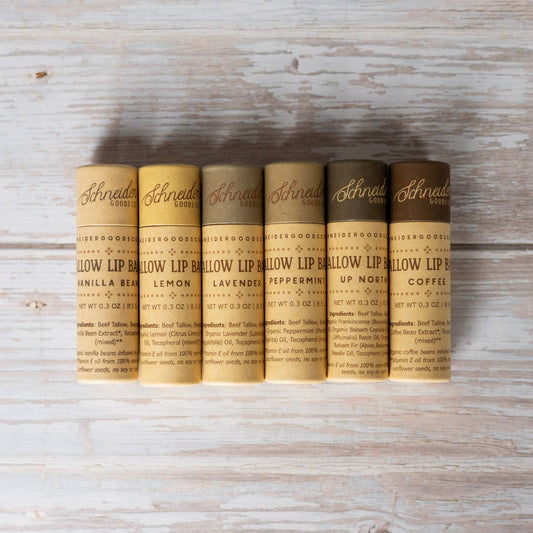 Six tallow lip balm scents in large compostable tubes on a wood background.