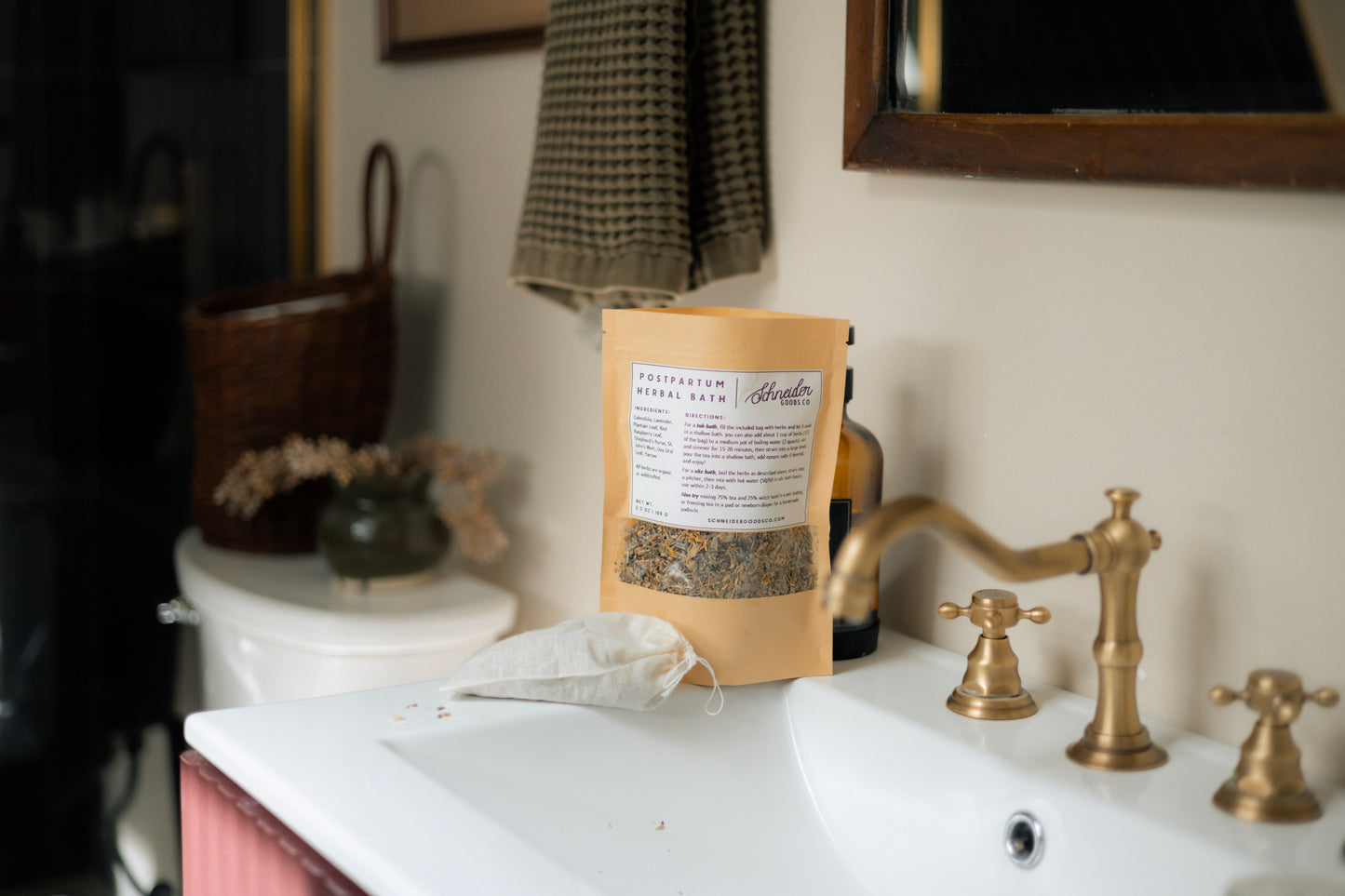 Open paper bag of postpartum herbal sitz bath sits on a white counter, with filled muslin herb bag next to it.