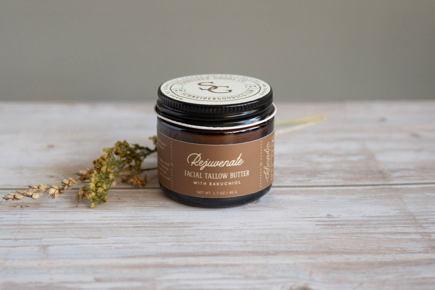 Jar of Rejuvenate facial tallow with bakuchiol on a wooden surface with dried herbs.