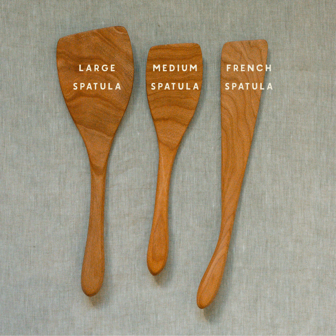 Three wooden kitchen spatulas in different sizes labeled 'LARGE SPATULA', 'MEDIUM SPATULA', and 'FRENCH SPATULA' on a textured light gray background.