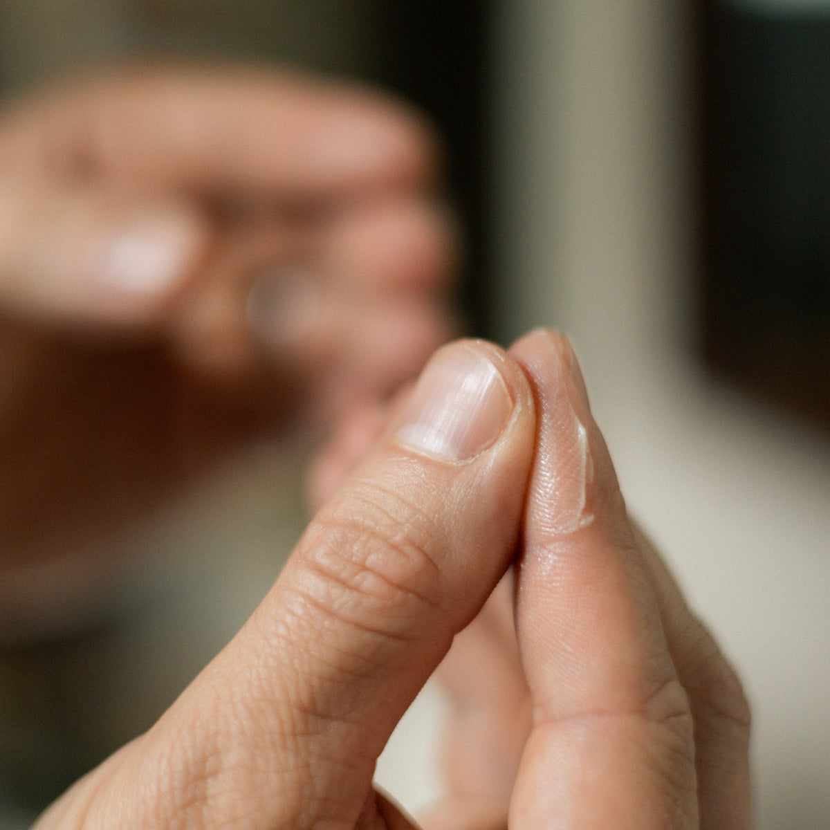 A close-up of a person's hand melting tallow hair clay between the thumb and index finger, with a blurred background showing another hand.