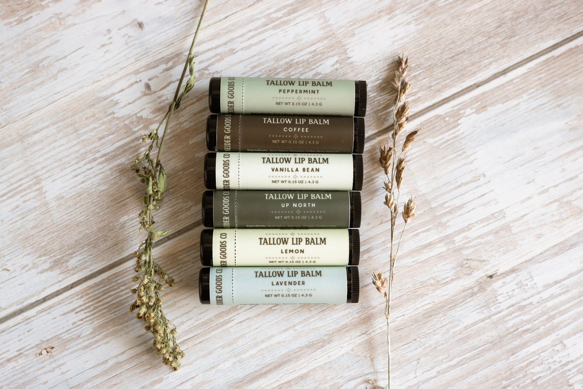 Set of Tallow Lip Balm tubes on a wooden surface with dried herbs.