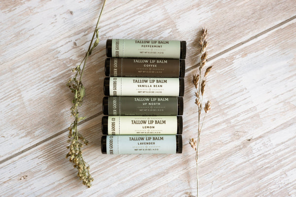 Set of Tallow Lip Balm tubes on a wooden surface with dried herbs.