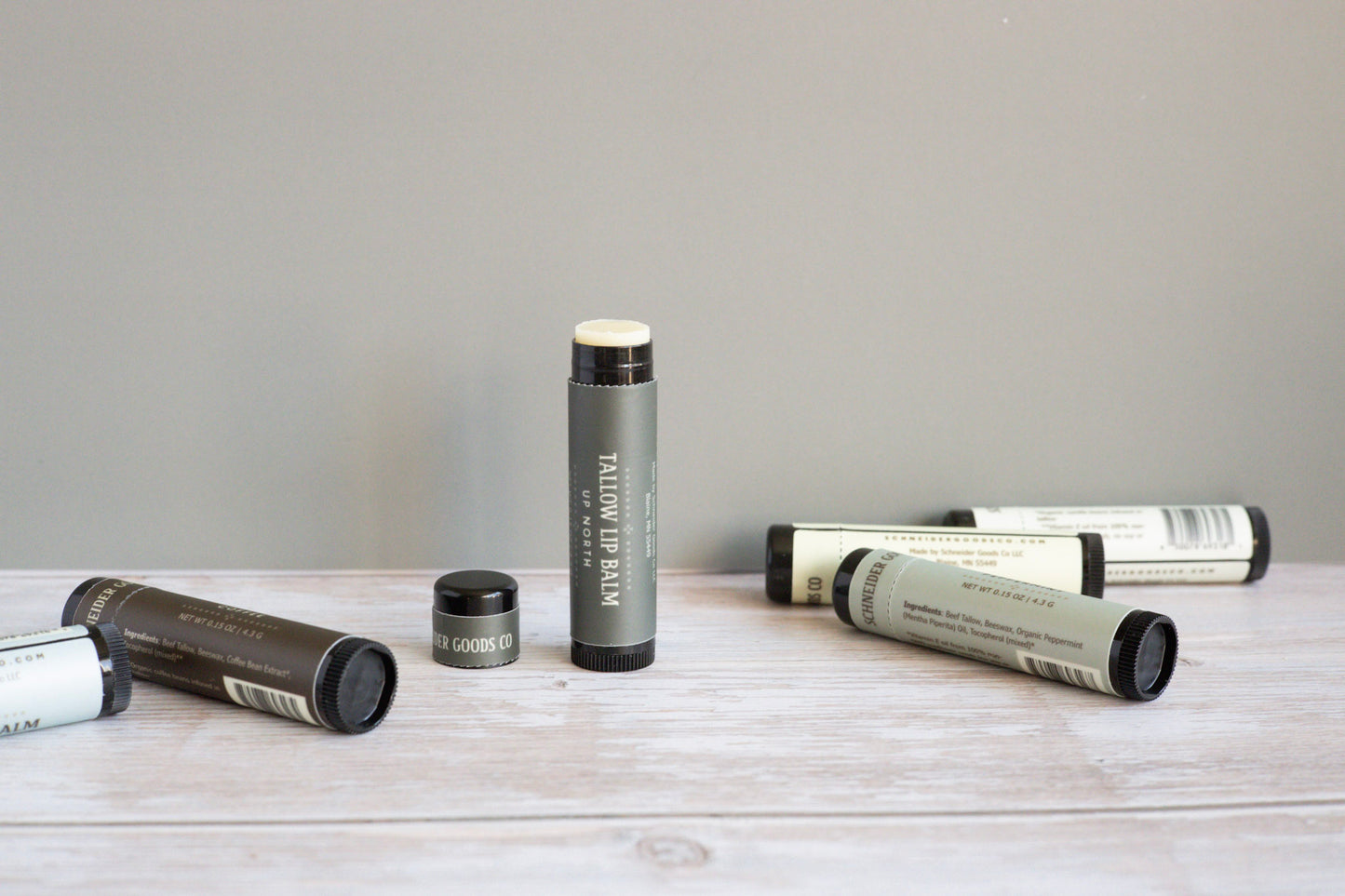 Collection of tallow lip balm tubes on a wooden surface with a gray background