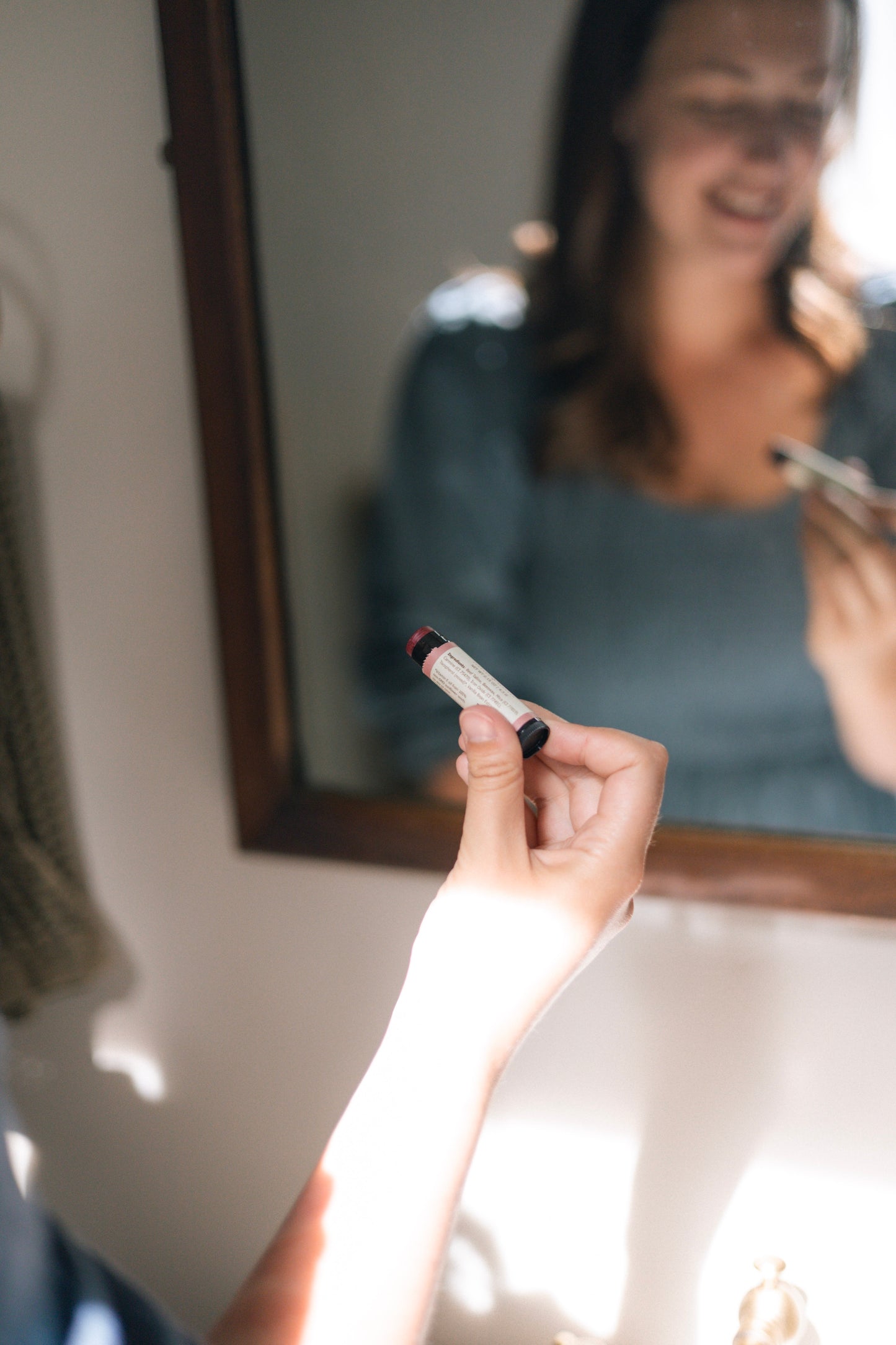 Person holding a tinted tallow lip balm in front of a mirror