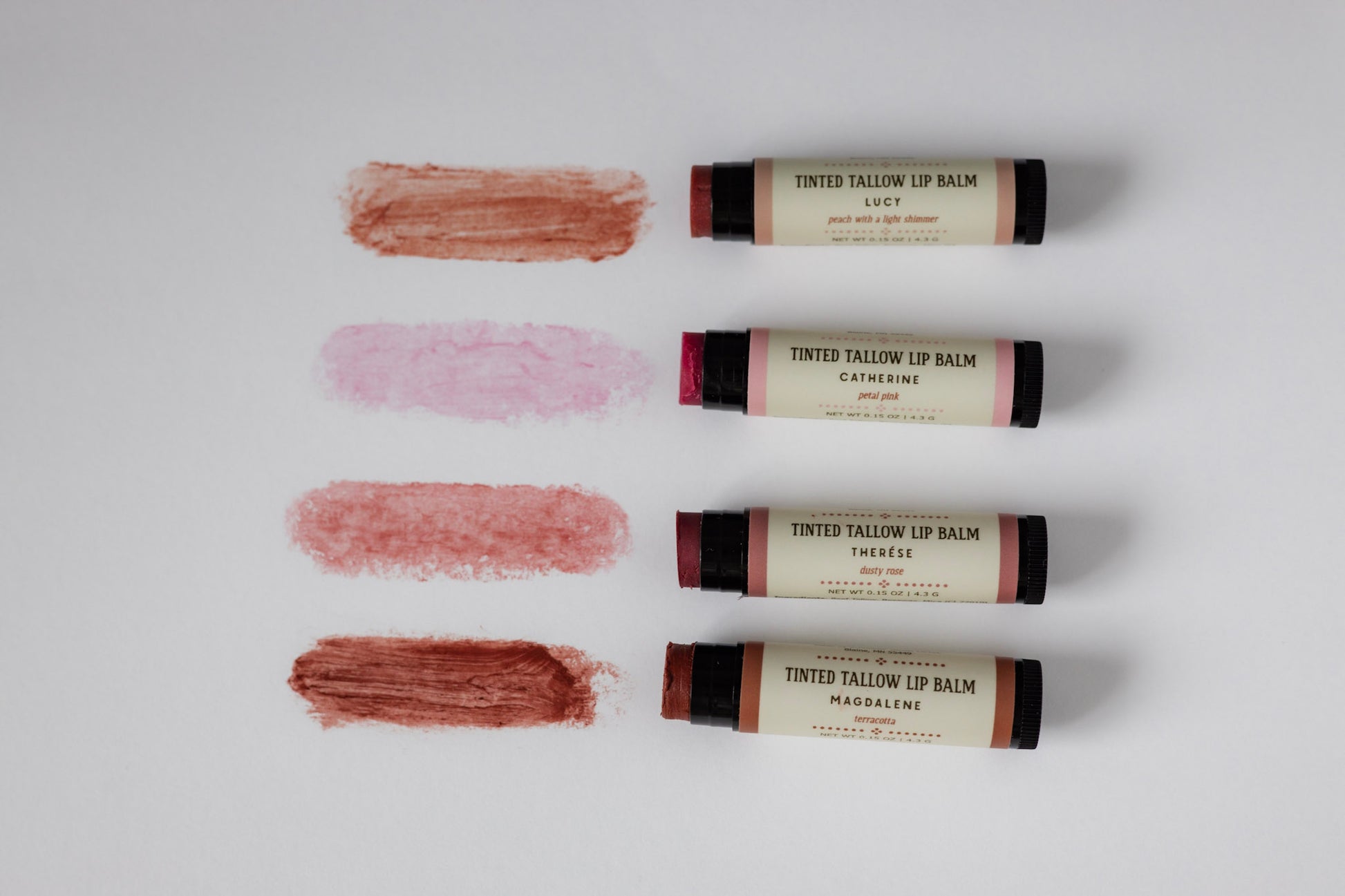 Four tinted lip balm sticks with swatches on a white background