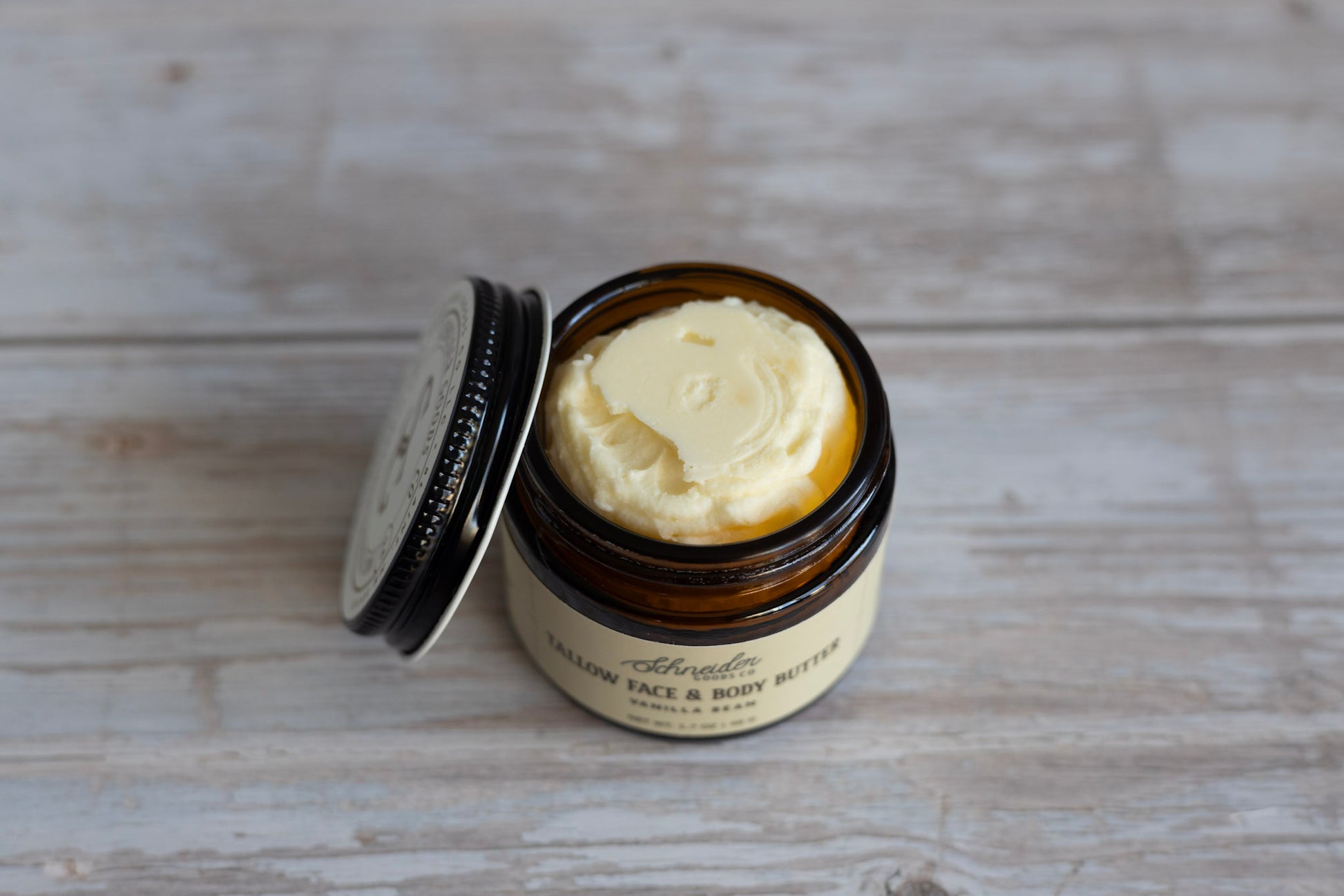 Jar of tallow face and body butter on a wooden surface