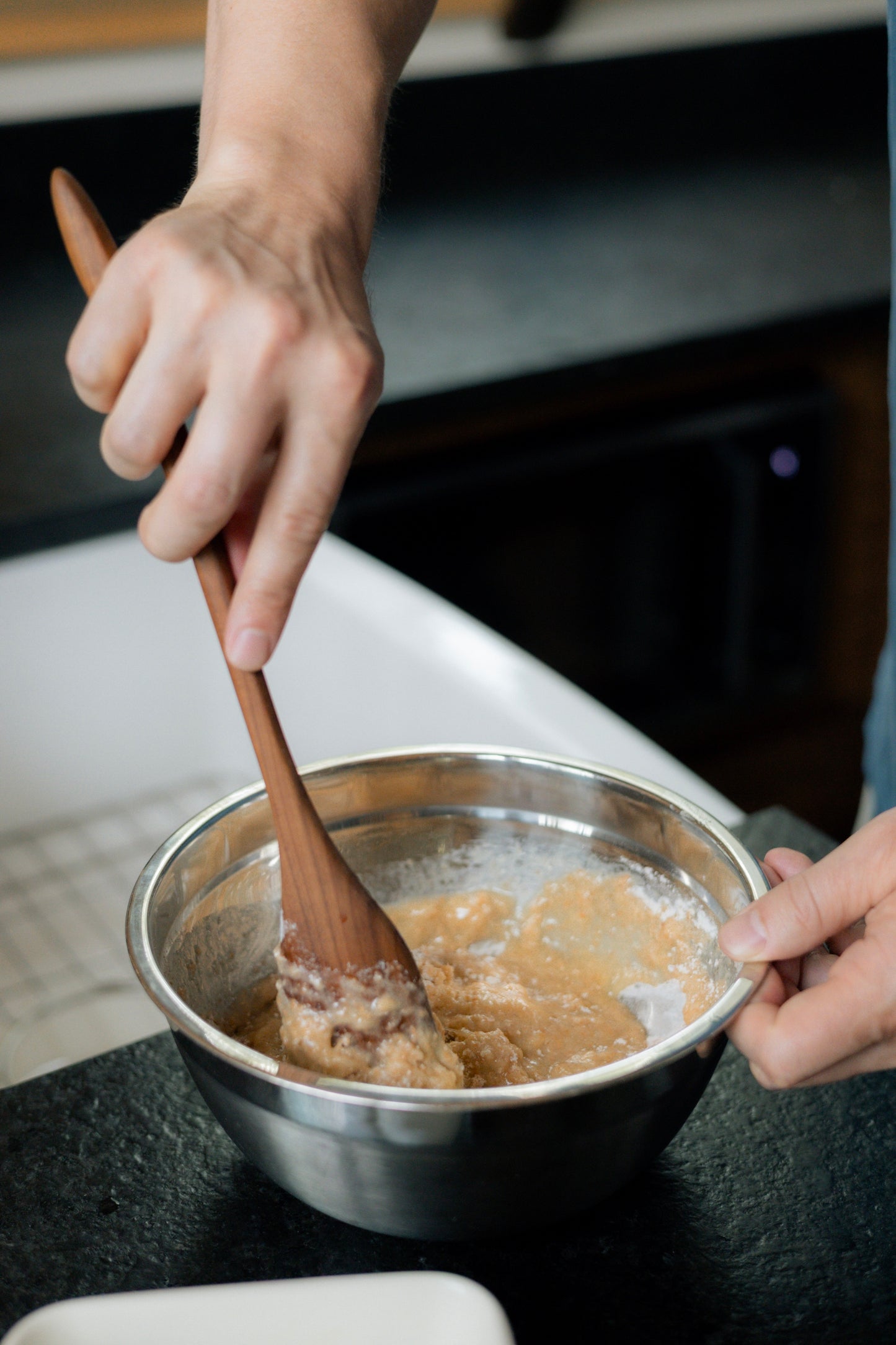 Cherry wood spoon stirring mix in silver bowl.