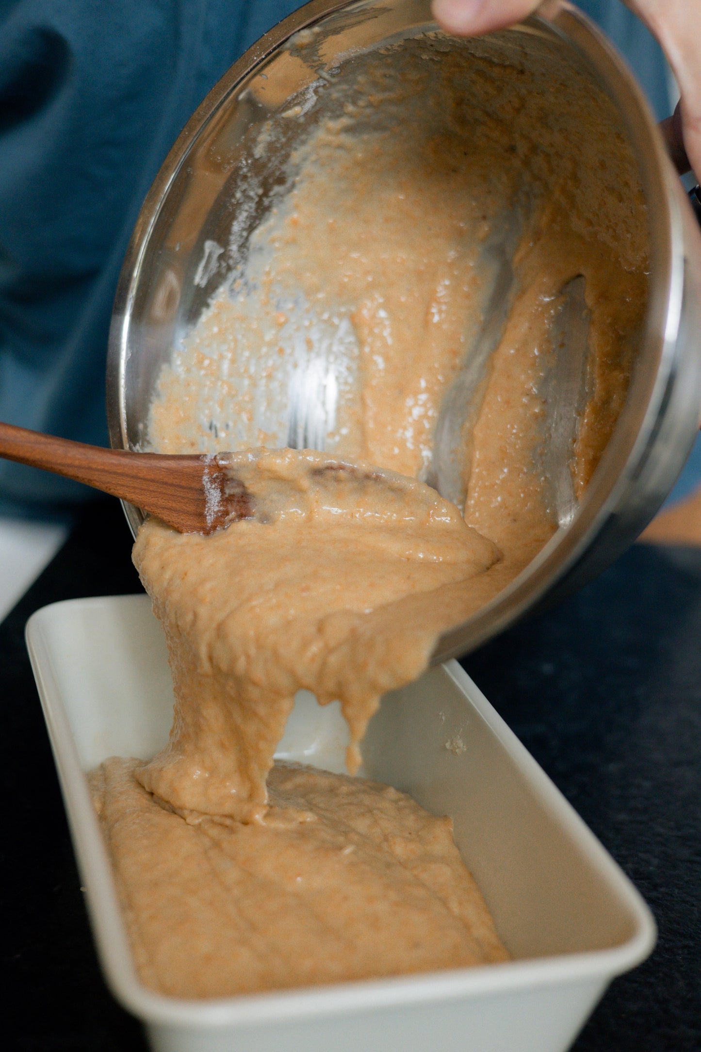 Cherry wood spoon pouring out mix into bread pan.