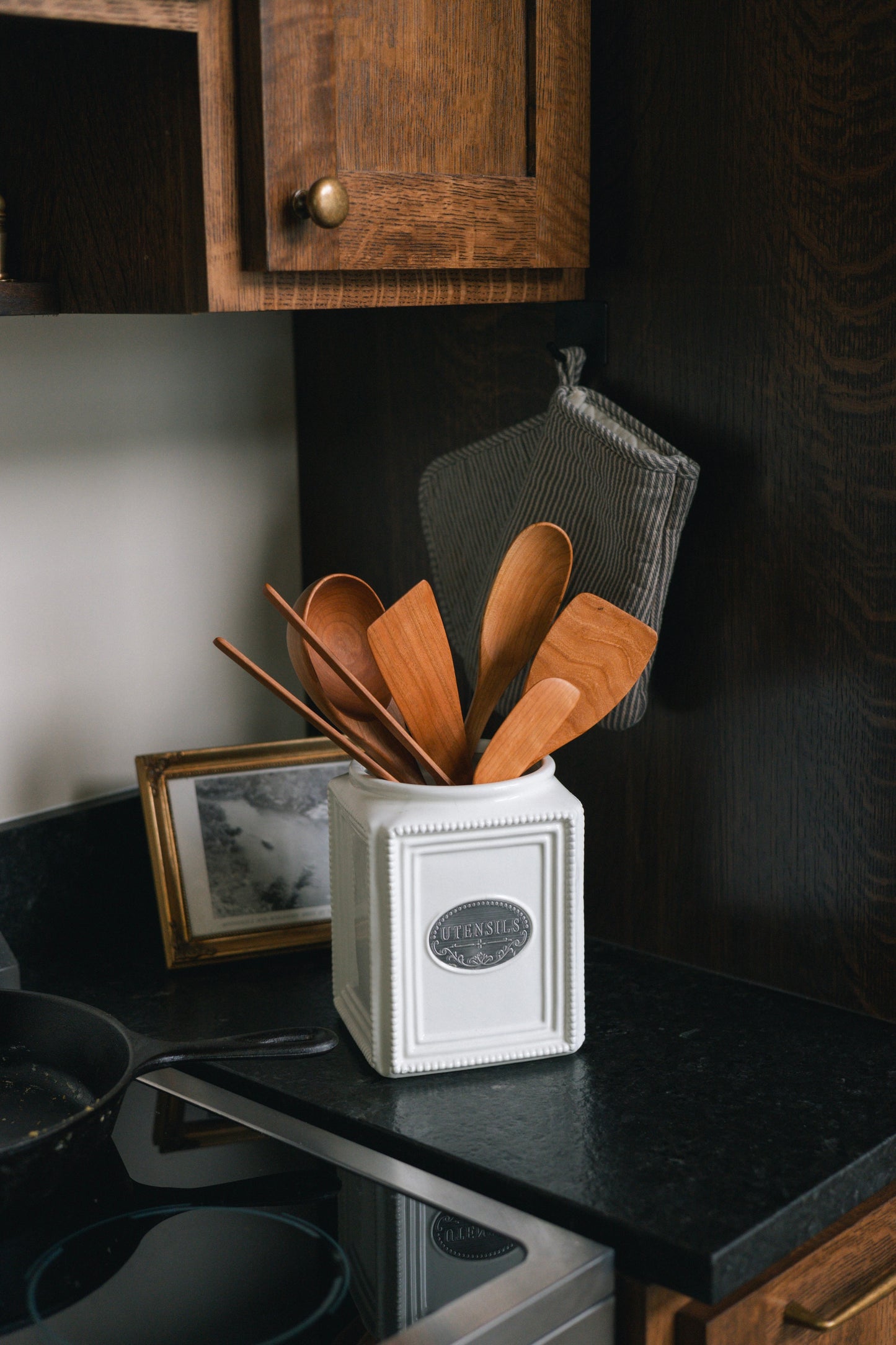 White utensil crock on counter with  cherry wood cooking utensils